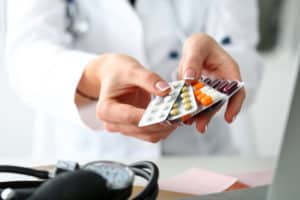 imagem de um profissional da saúde segurando nas duas mãos várias cartelas de remédios